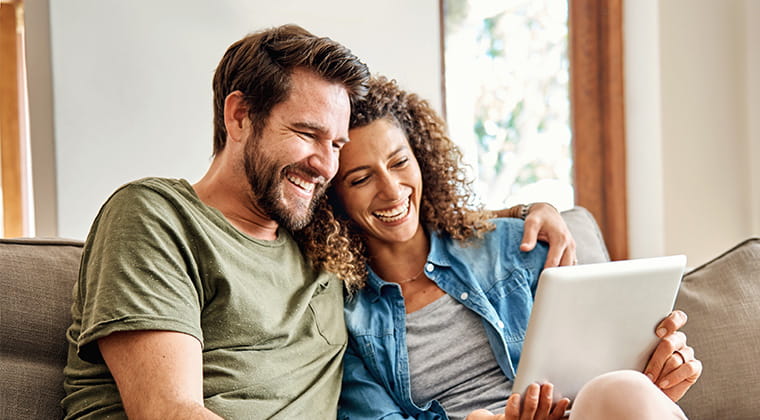 A couple sits on a couch and looks at the tablet